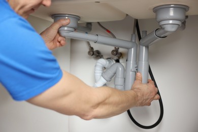 Photo of Plumber fixing pipes under sink indoors, closeup