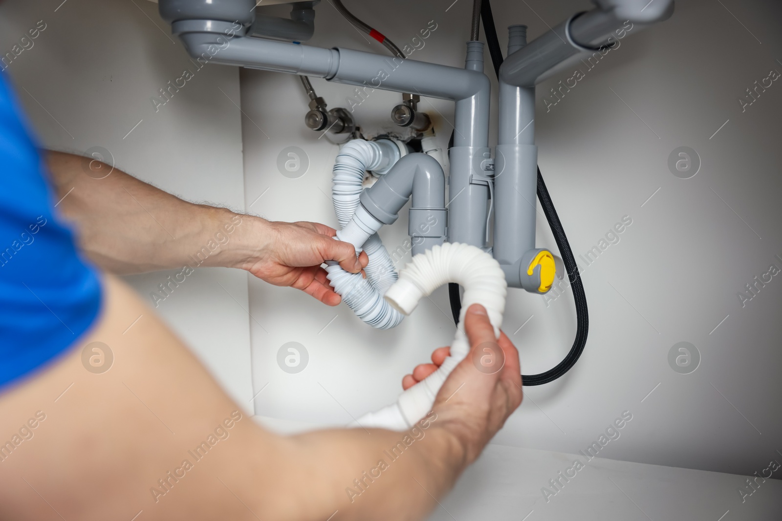 Photo of Plumber fixing pipes under sink indoors, closeup
