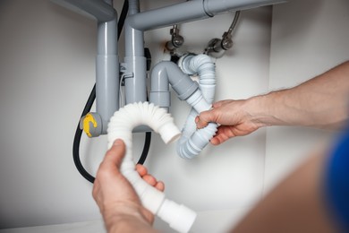 Photo of Plumber fixing pipes under sink indoors, closeup