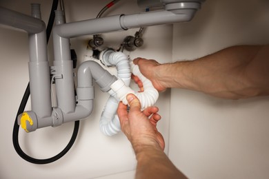 Photo of Plumber fixing pipes under sink indoors, closeup