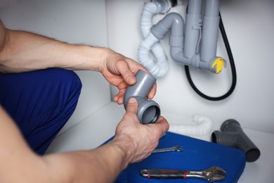 Photo of Plumber fixing pipes under sink indoors, closeup