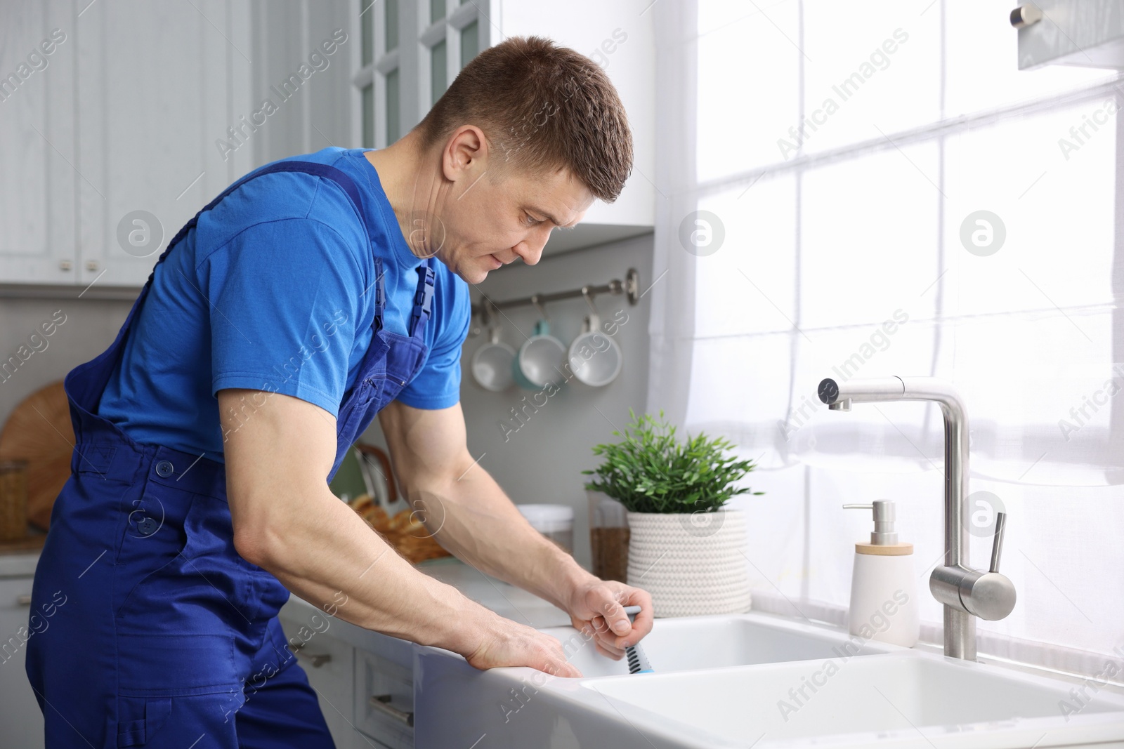 Plumber unclogging sink with hand plunger indoors Photo of Plumber unclogging sink with hand plunger indoors