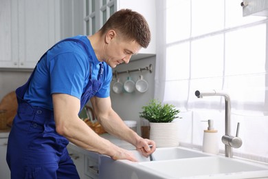 Photo of Plumber unclogging sink with hand plunger indoors