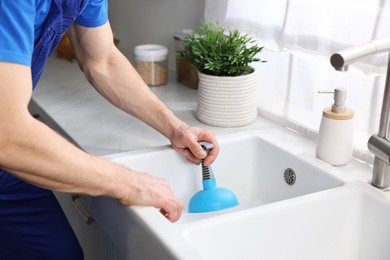 Photo of Plumber unclogging sink with hand plunger indoors, closeup