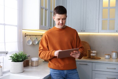 Photo of Man using modern tablet in kitchen at home
