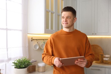 Photo of Man using modern tablet in kitchen at home