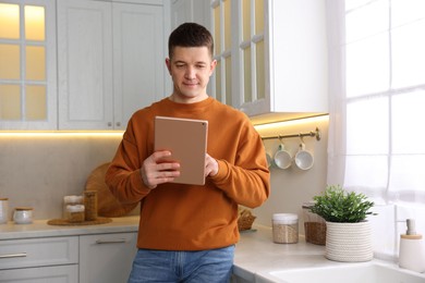 Photo of Man using modern tablet in kitchen at home