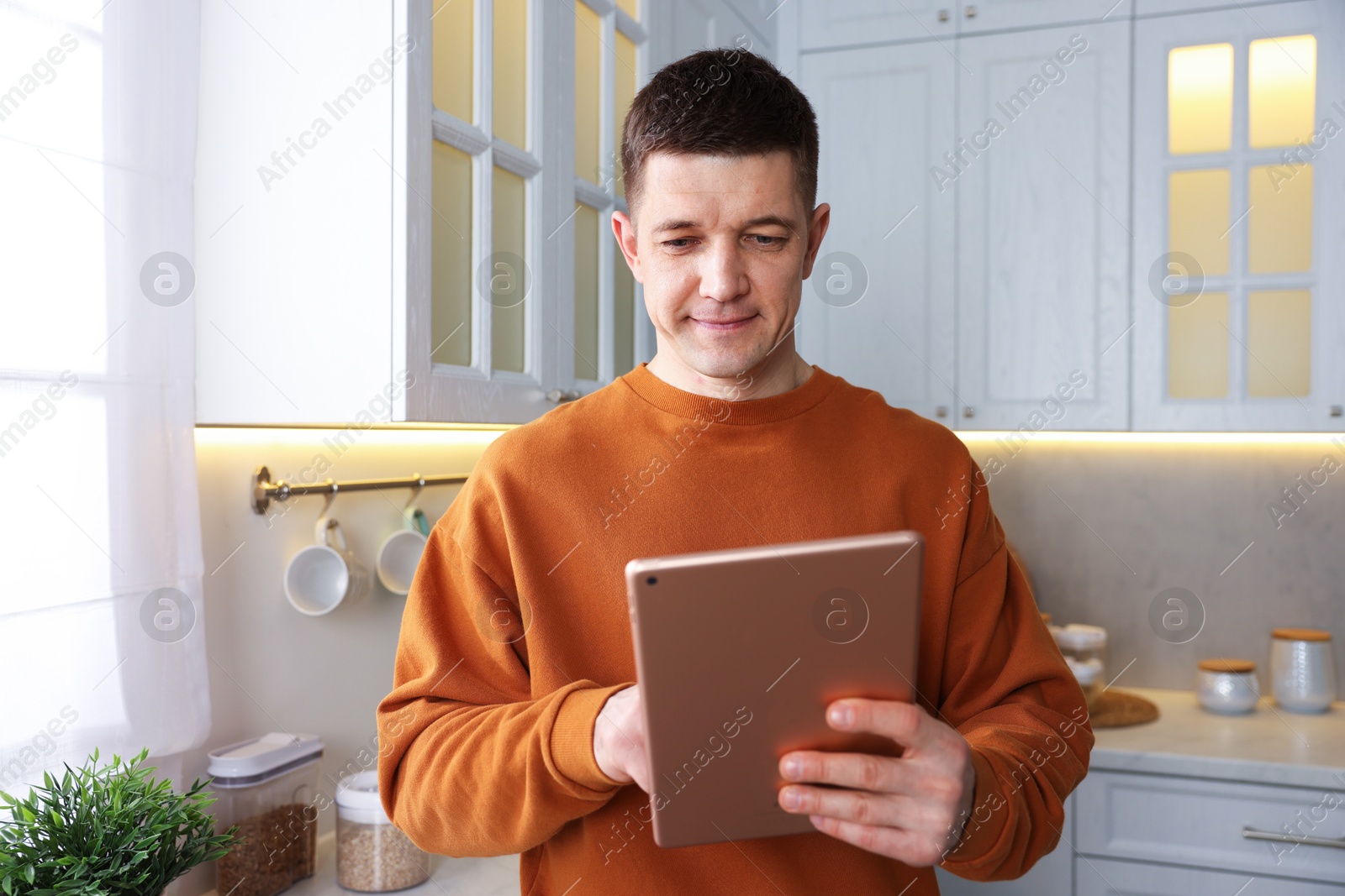 Man using modern tablet in kitchen at home Photo of Man using modern tablet in kitchen at home