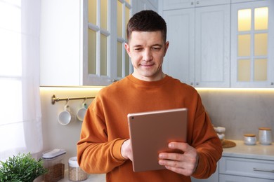 Photo of Man using modern tablet in kitchen at home