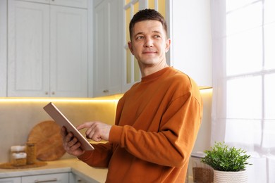 Photo of Man using modern tablet in kitchen at home