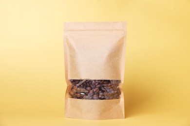 Photo of One zipper stand-up pouch with coffee beans on light orange background. Mockup for design