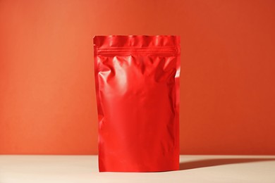 Photo of One zipper stand-up pouch on white table against red background. Mockup for design