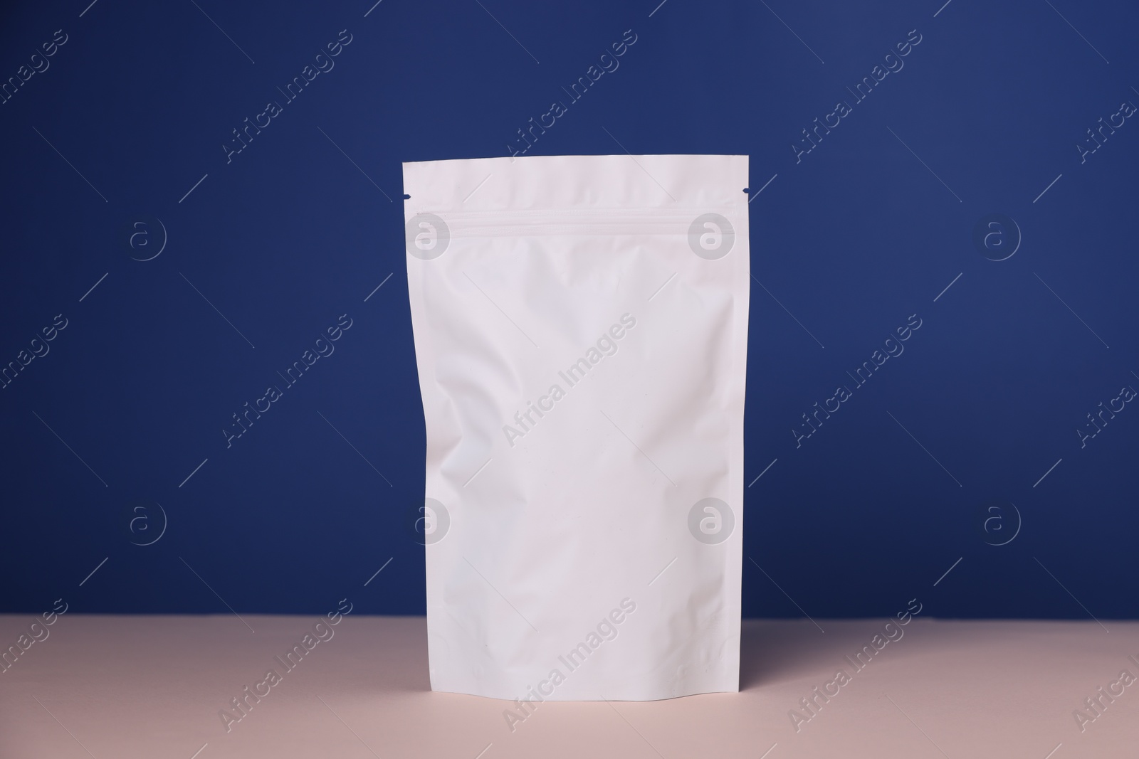 Photo of One zipper stand-up pouch on pink table against blue background. Mockup for design