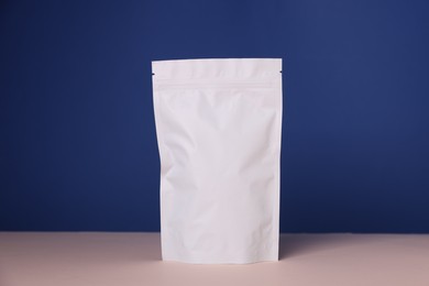 Photo of One zipper stand-up pouch on pink table against blue background. Mockup for design