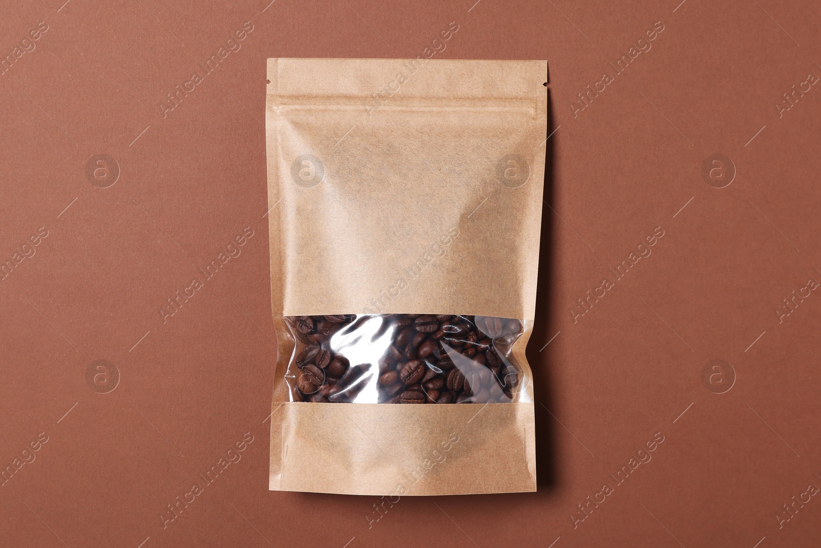 Photo of One zipper stand-up pouch with coffee beans on brown background, top view. Mockup for design
