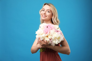 Photo of Happy woman with bouquet of beautiful peonies on light blue background