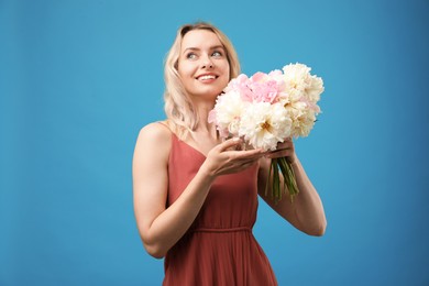 Photo of Happy woman with bouquet of beautiful peonies on light blue background