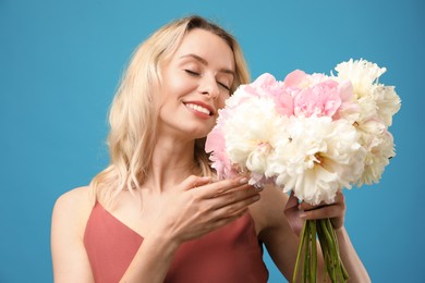 Photo of Happy woman with bouquet of beautiful peonies on light blue background