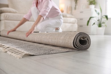 Photo of Woman putting new rug on floor at home, closeup