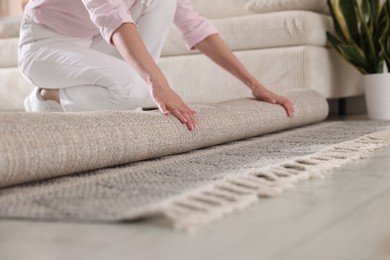 Photo of Woman putting new rug on floor at home, closeup