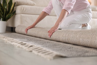 Photo of Woman putting new rug on floor at home, closeup