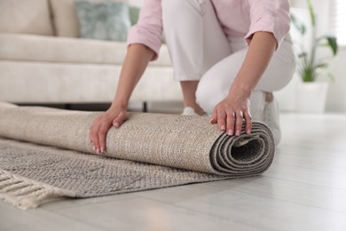 Photo of Woman putting new rug on floor at home, closeup