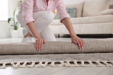 Photo of Woman putting new rug on floor at home, closeup