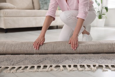 Photo of Woman putting new rug on floor at home, closeup