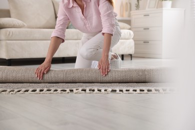 Photo of Woman putting new rug on floor at home, closeup
