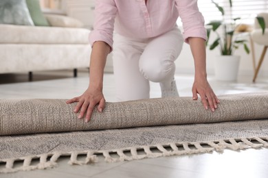 Photo of Woman putting new rug on floor at home, closeup