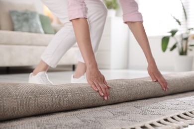 Photo of Woman putting new rug on floor at home, closeup