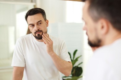 Photo of Handsome man before shaving looking at mirror in bathroom