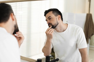 Photo of Handsome man before shaving looking at mirror in bathroom
