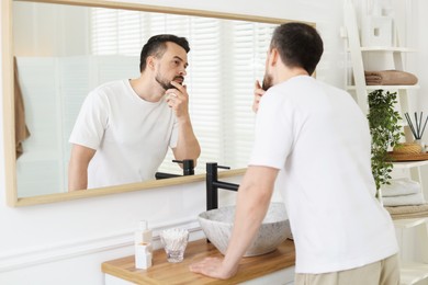 Photo of Handsome man before shaving looking at mirror in bathroom