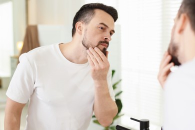 Photo of Handsome man before shaving looking at mirror in bathroom