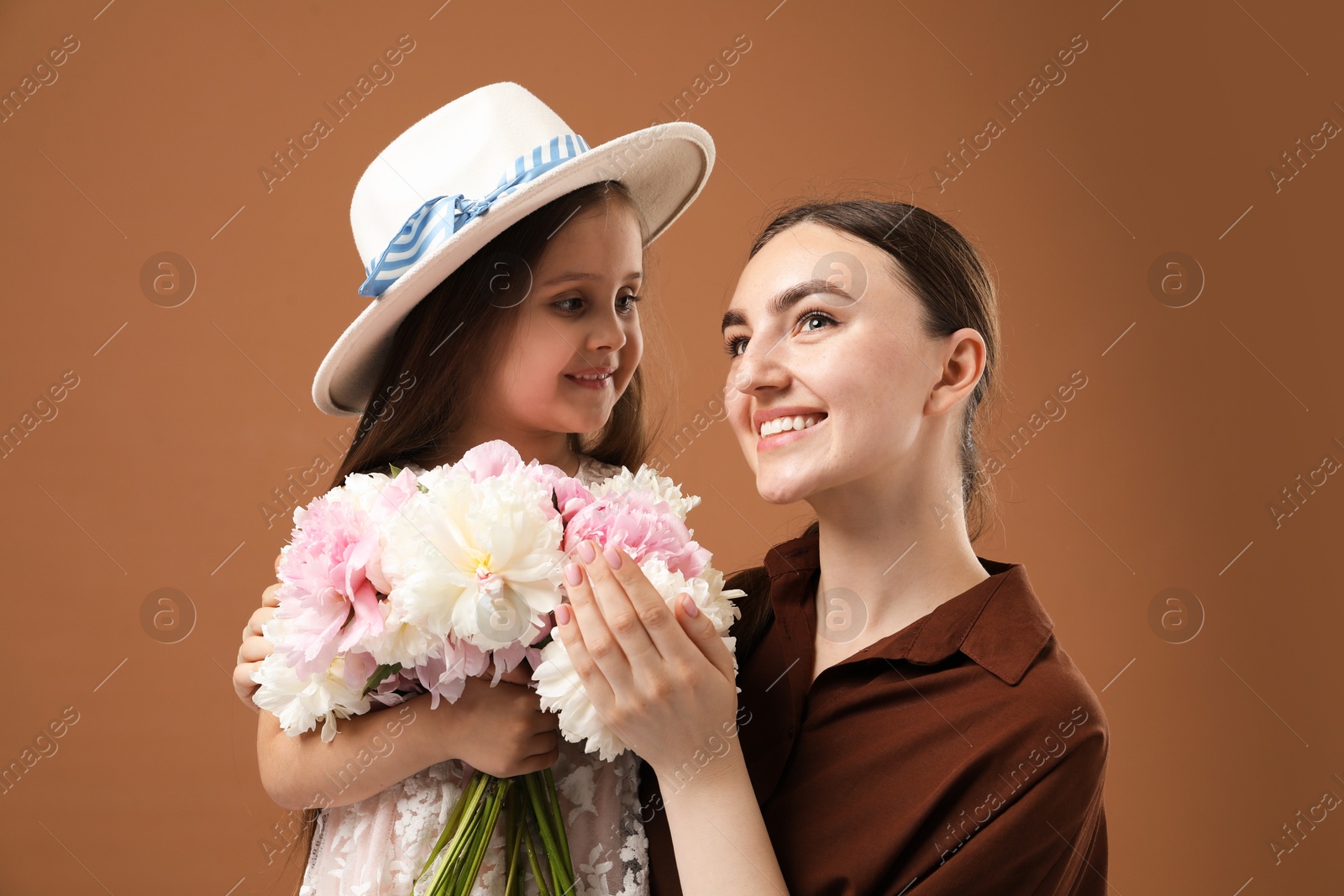 Mother and her daughter with bouquet of beautiful peonies on brown background Photo of Mother and her daughter with bouquet of beautiful peonies on brown background