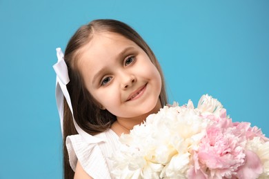 Photo of Cute little girl with bouquet of beautiful peonies on light blue background