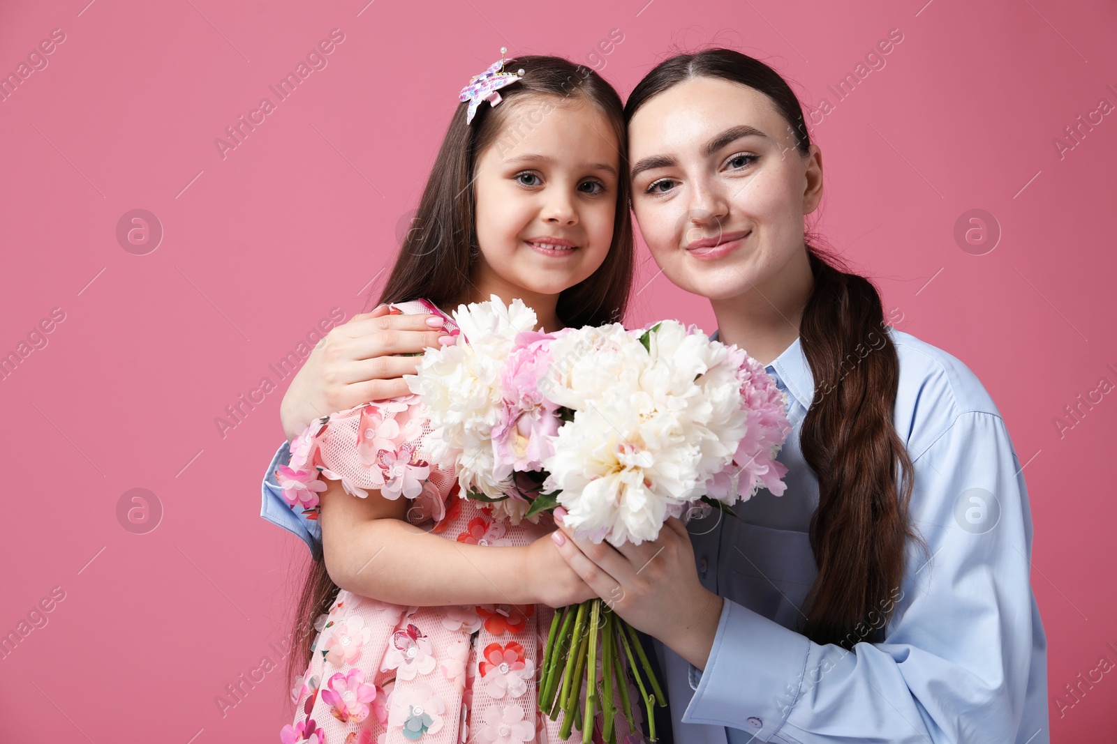 Mother and her daughter with bouquet of beautiful peonies on pink background Photo of Mother and her daughter with bouquet of beautiful peonies on pink background