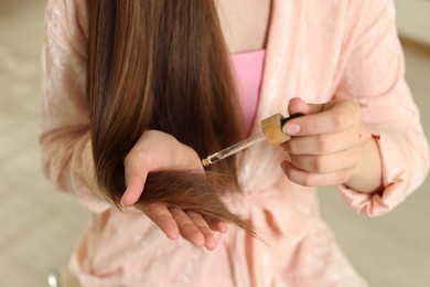 Photo of Teenage girl applying serum onto her hair at home, closeup
