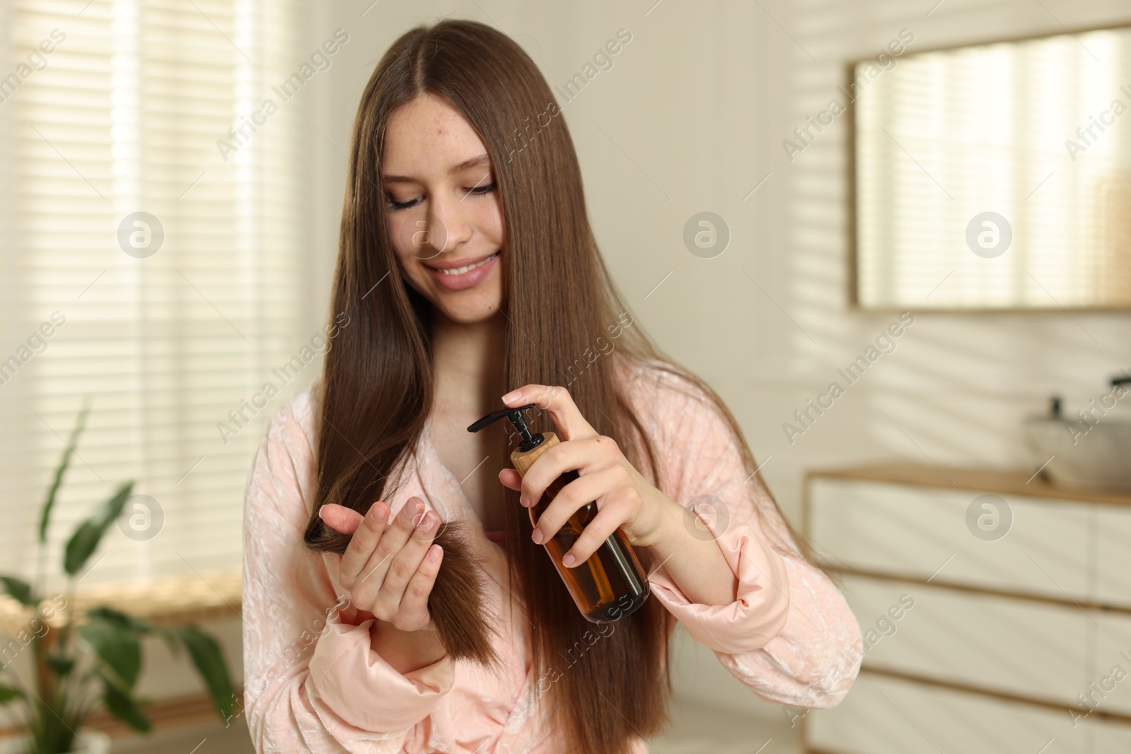 Smiling teenage girl applying cosmetic product onto her hair at home Photo of Smiling teenage girl applying cosmetic product onto her hair at home