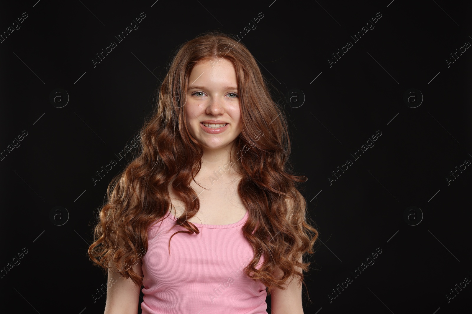 Smiling teenage girl with healthy wavy hair on black background Photo of Smiling teenage girl with healthy wavy hair on black background