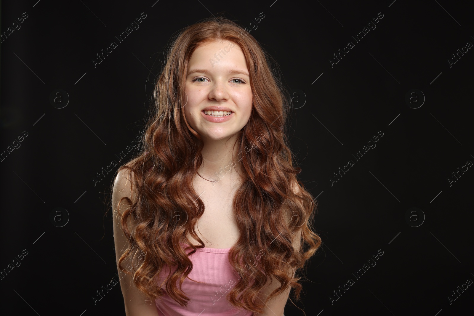 Portrait of smiling teenage girl with healthy wavy hair on black background Photo of Portrait of smiling teenage girl with healthy wavy hair on black background