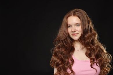 Photo of Beautiful teenage girl with healthy wavy hair on black background. Space for text