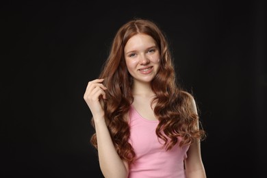 Photo of Smiling teenage girl with healthy wavy hair on black background. Space for text