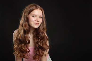 Photo of Beautiful teenage girl with healthy wavy hair on black background. Space for text