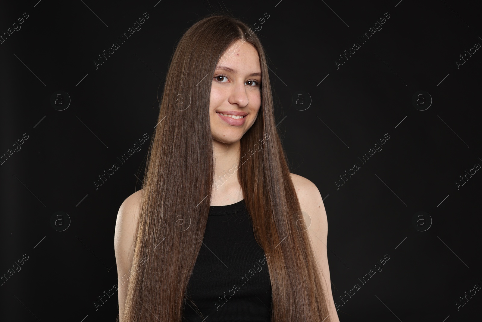 Portrait of smiling teenage girl with healthy long hair on black background Photo of Portrait of smiling teenage girl with healthy long hair on black background