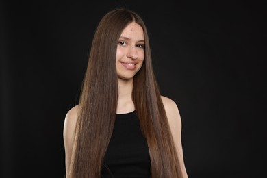 Photo of Portrait of smiling teenage girl with healthy long hair on black background
