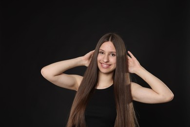 Photo of Portrait of smiling teenage girl with healthy long hair on black background