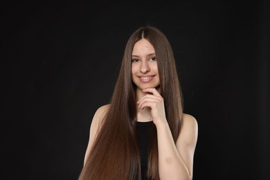 Photo of Portrait of smiling teenage girl with healthy long hair on black background