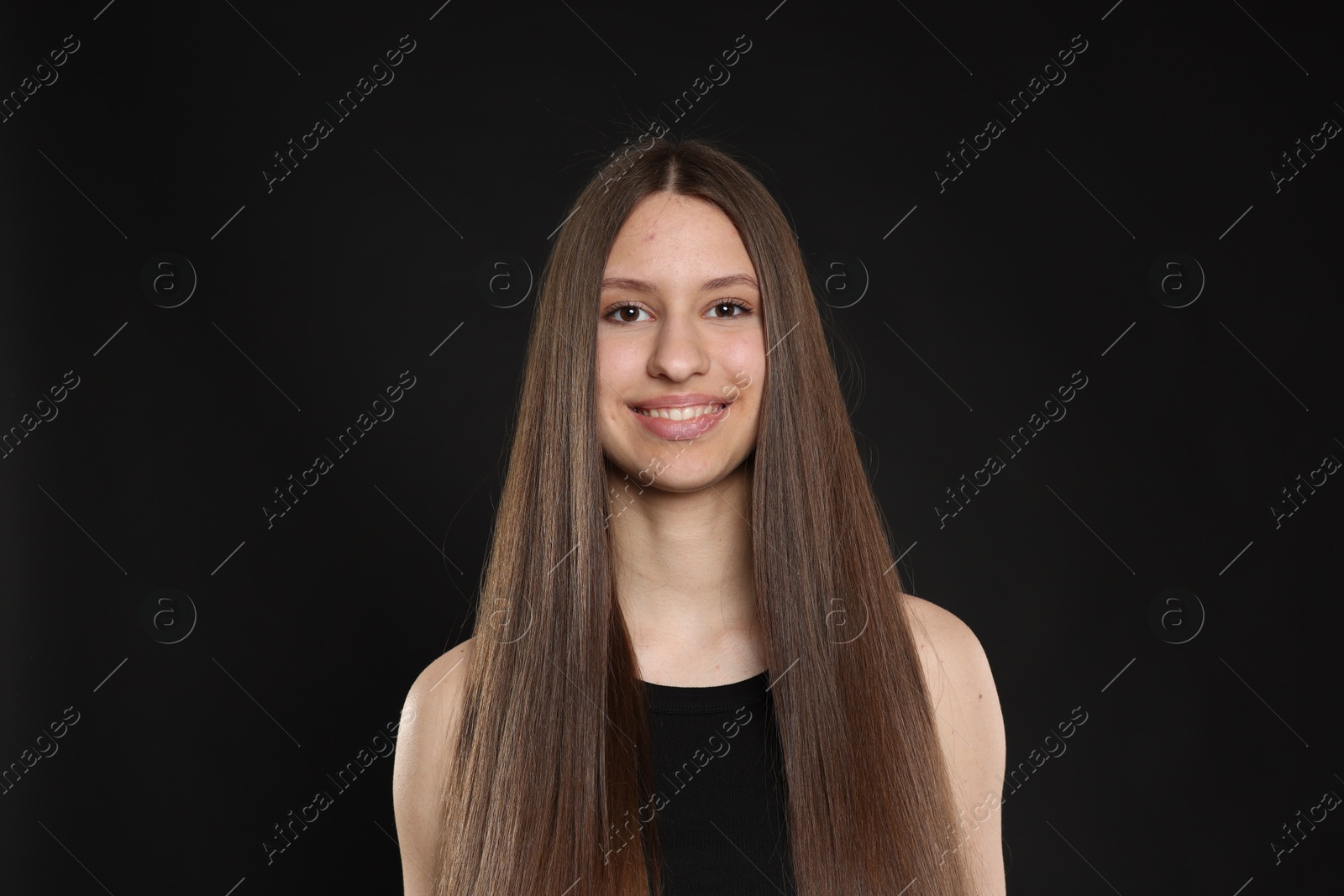 Portrait of smiling teenage girl with healthy long hair on black background Photo of Portrait of smiling teenage girl with healthy long hair on black background